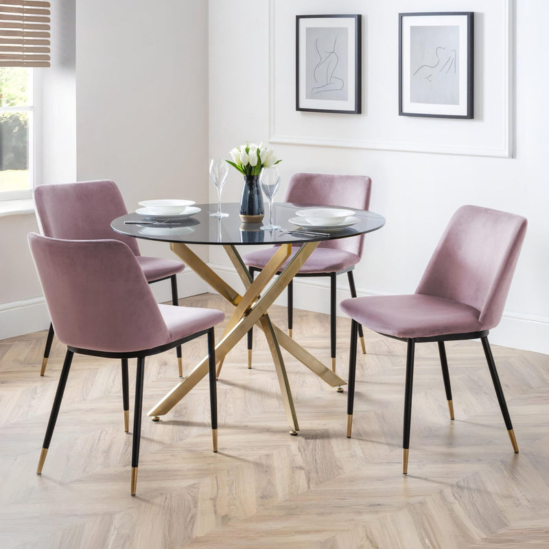 Dining room with a round glass table and four pink chairs on a wooden floor.