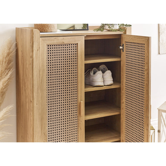 Wooden cabinet with wicker doors containing white shoes, placed against a neutral wall.