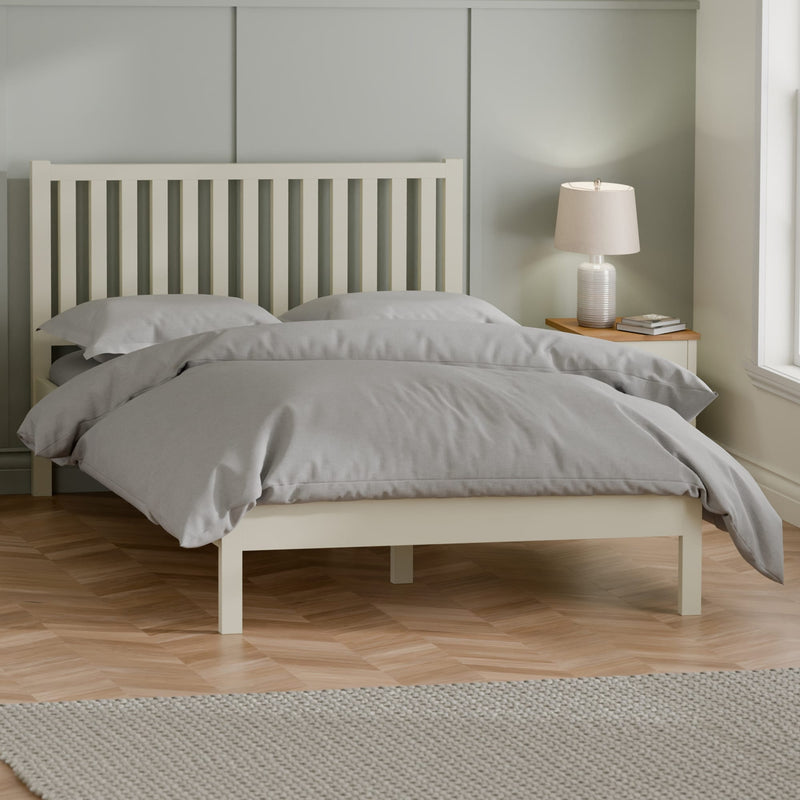 Neatly made bed with gray bedding in a room with a lamp and window.