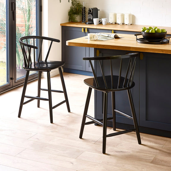 Two black bar stools in a kitchen setting with a wooden counter and cabinets.