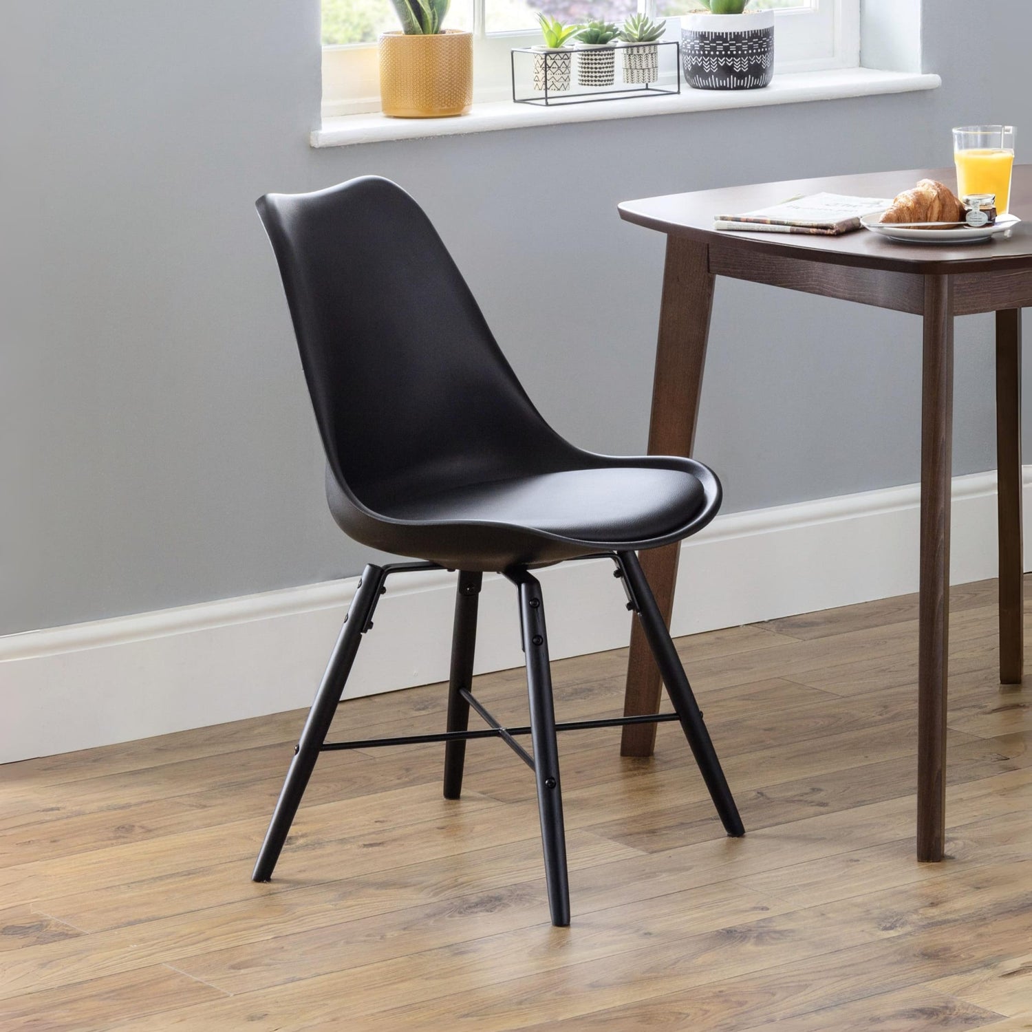 Black chair in a room with a wooden table and window sill with plants.