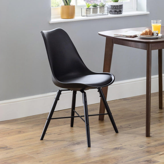 Black chair in a room with a wooden table and window sill with plants.
