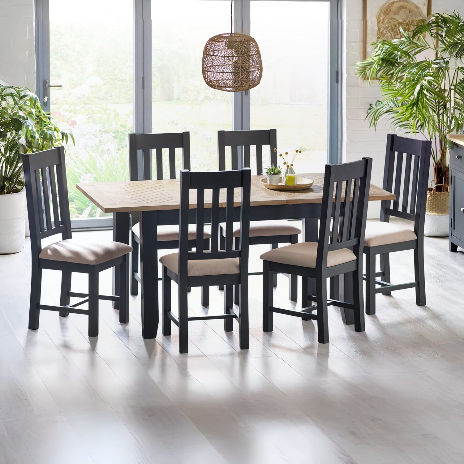 Dining room with a wooden table and black chairs with beige cushions, plants, and a lamp.