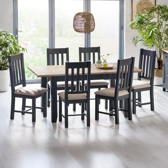 Dining room with a wooden table and black chairs with beige cushions, plants, and a lamp.