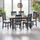 Dining room with a wooden table and black chairs with beige cushions, plants, and a lamp.