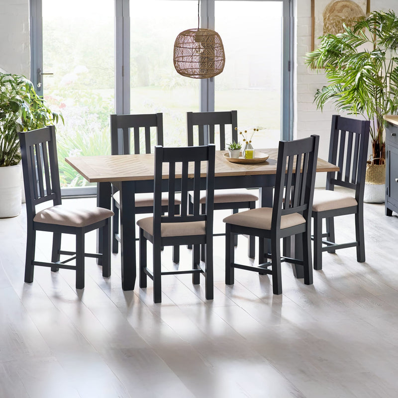 Dining room with a wooden table and black chairs with beige cushions, plants, and a lamp.