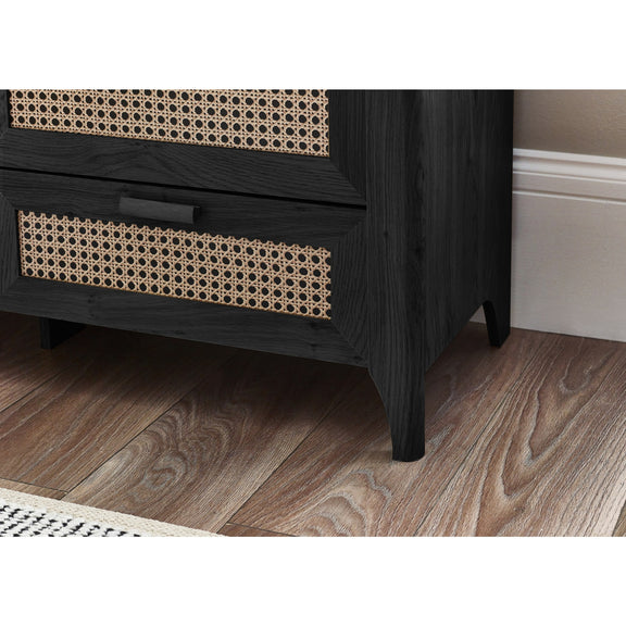 Black wooden dresser with woven patterns on drawers against a neutral wall.