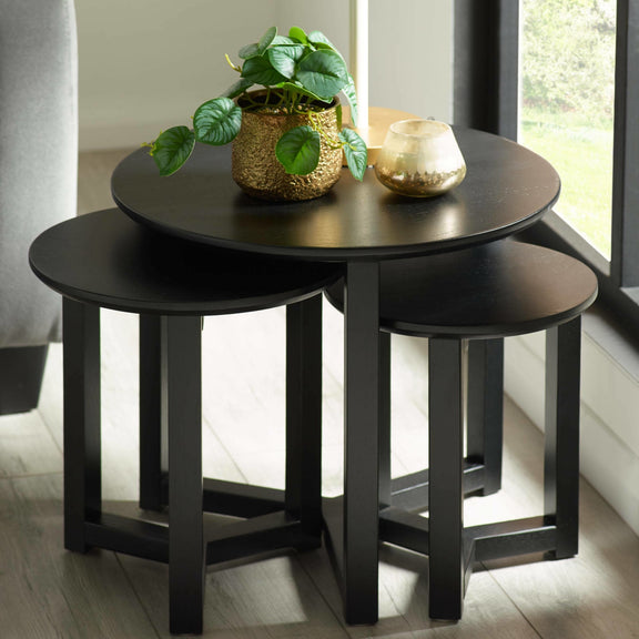 Set of three black nesting tables with a plant and candle on top in a bright room.