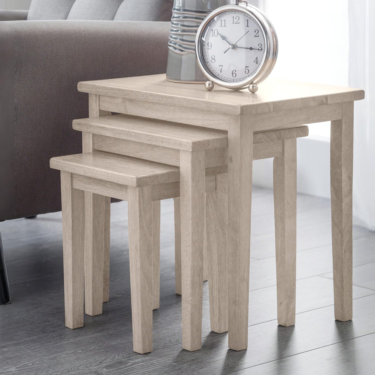 Set of three wooden nesting tables with a clock on top in a room setting.