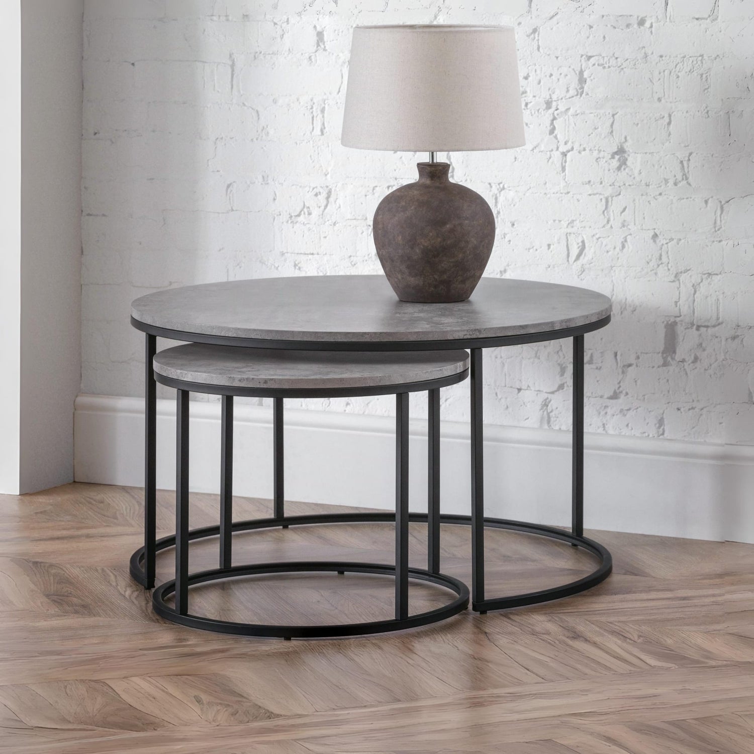 Set of two round tables with a lamp on top against a white brick wall.