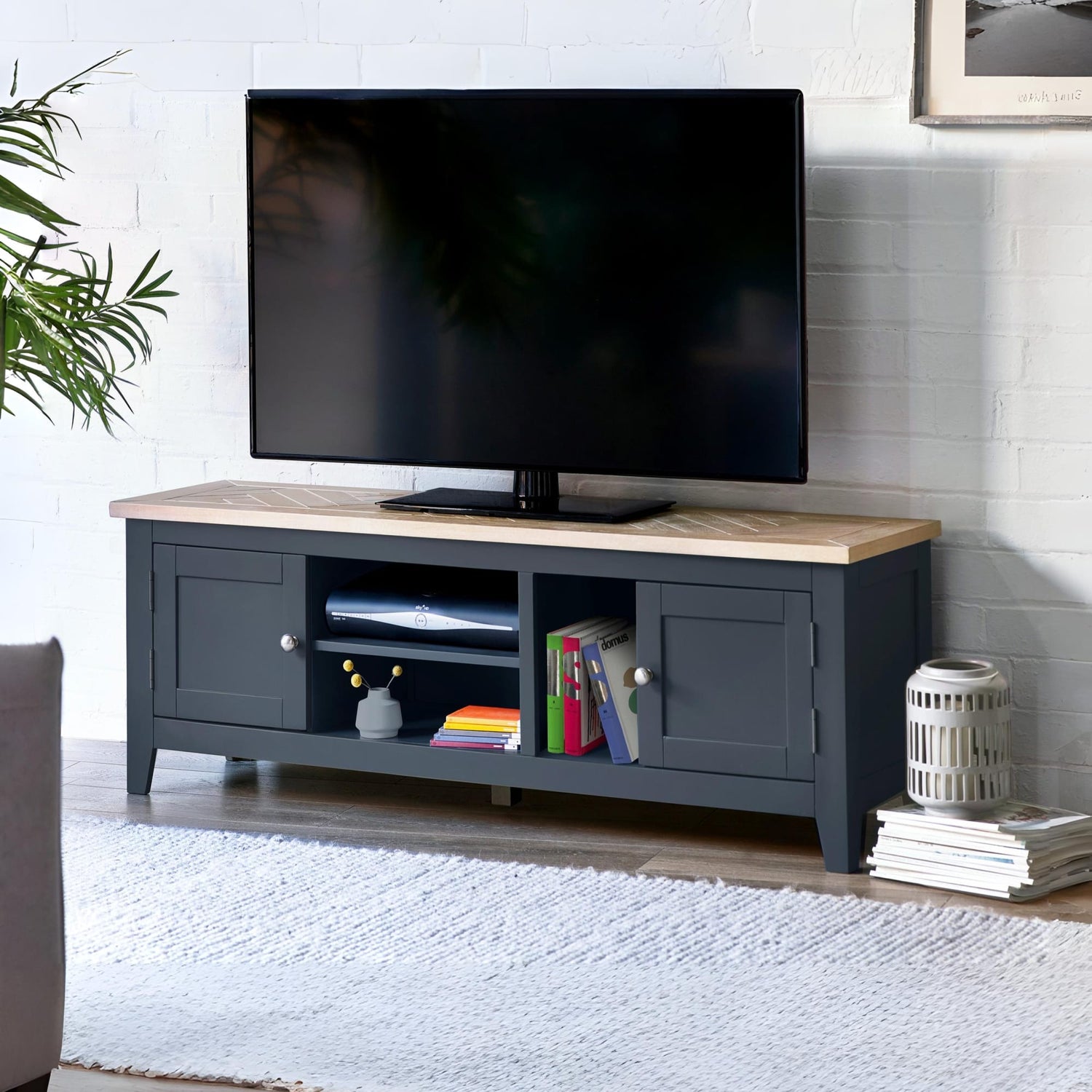 Black TV stand with a wooden top displaying a television, books, and decorative items in a living room setting.