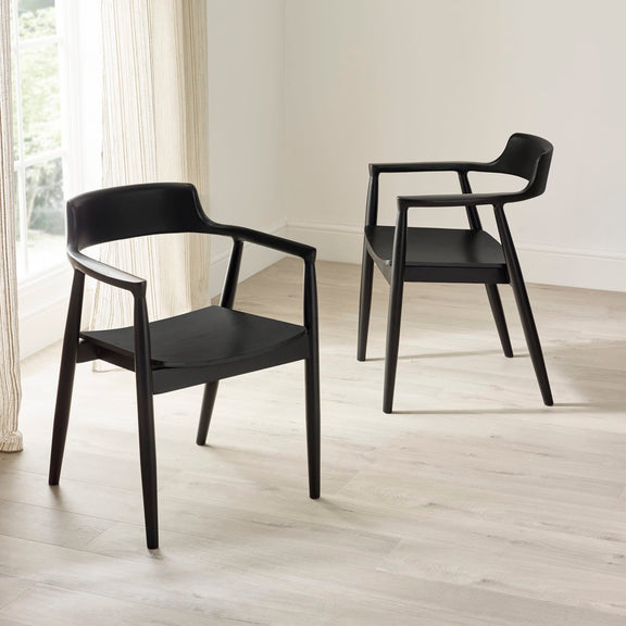 Two black chairs on a light wooden floor with a white wall background