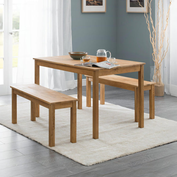 Wooden dining table with benches in a room with light blue walls and white curtains.