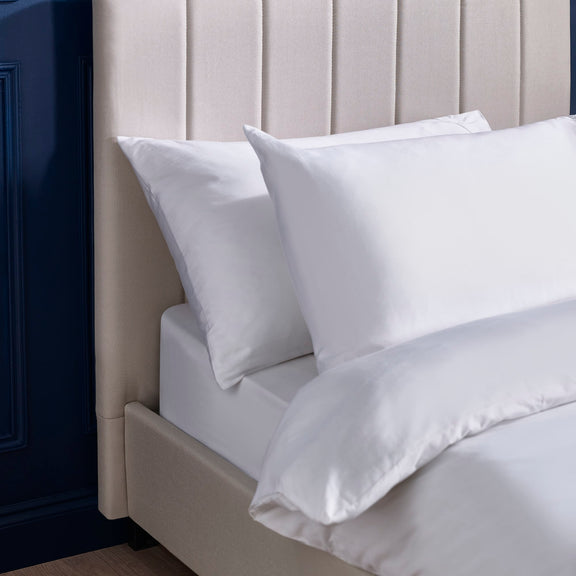 White bedding set on a bed with a neutral headboard.