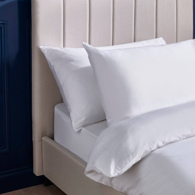 White bedding set on a bed with a neutral headboard.