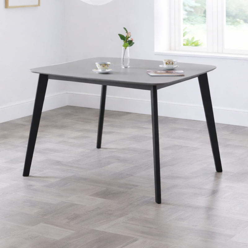 Dining table with a gray top and black legs in a room with a window.