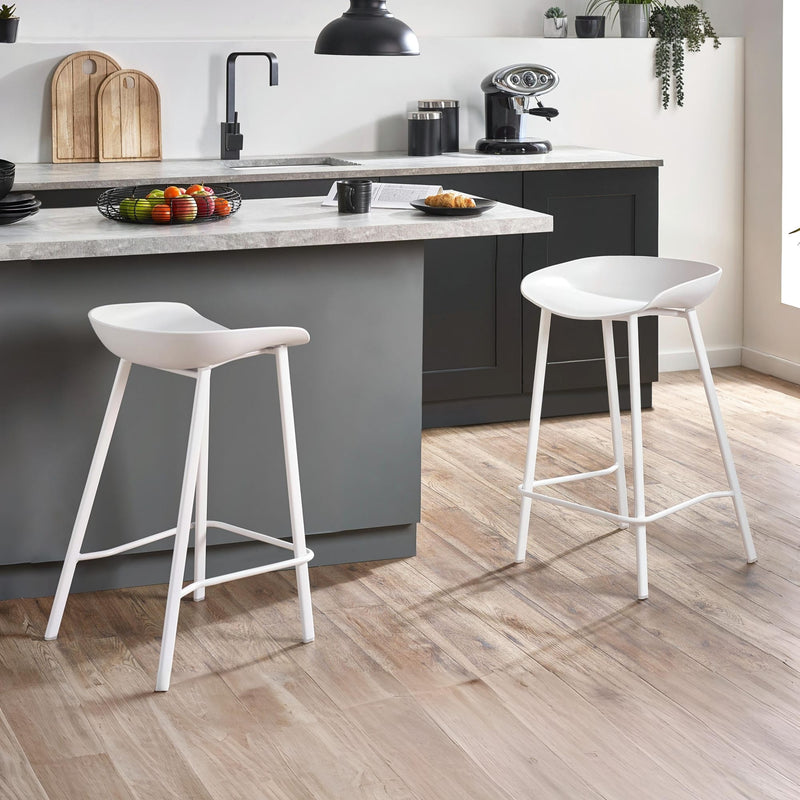 Modern kitchen with gray island, white stools, and wooden flooring.