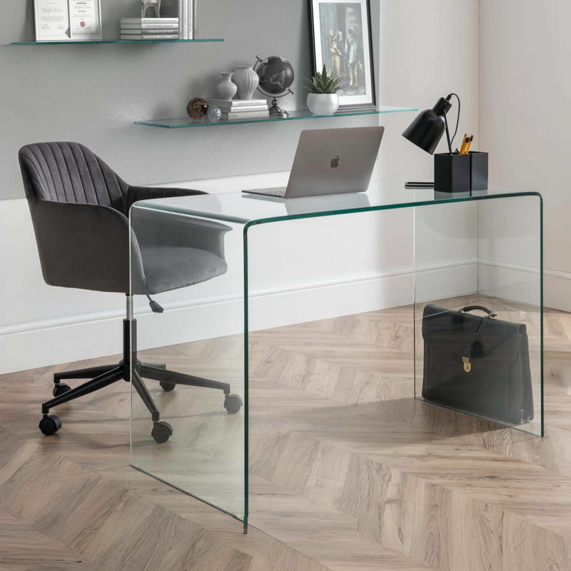 Modern home office with glass desk, gray chair, and decor items.