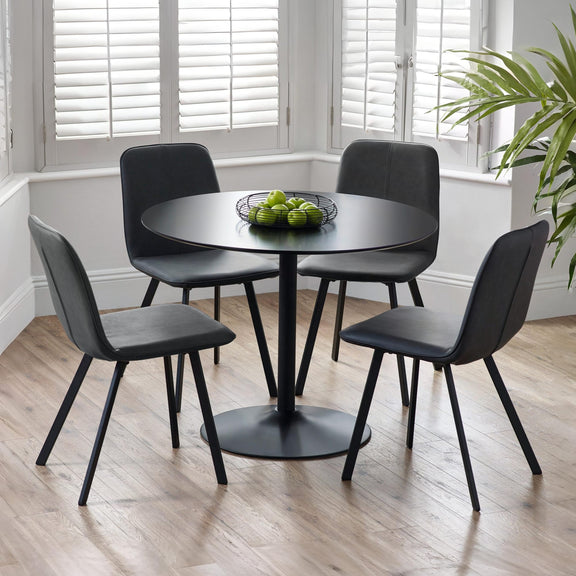 Black round dining table with four matching chairs in a room with large windows and a plant.