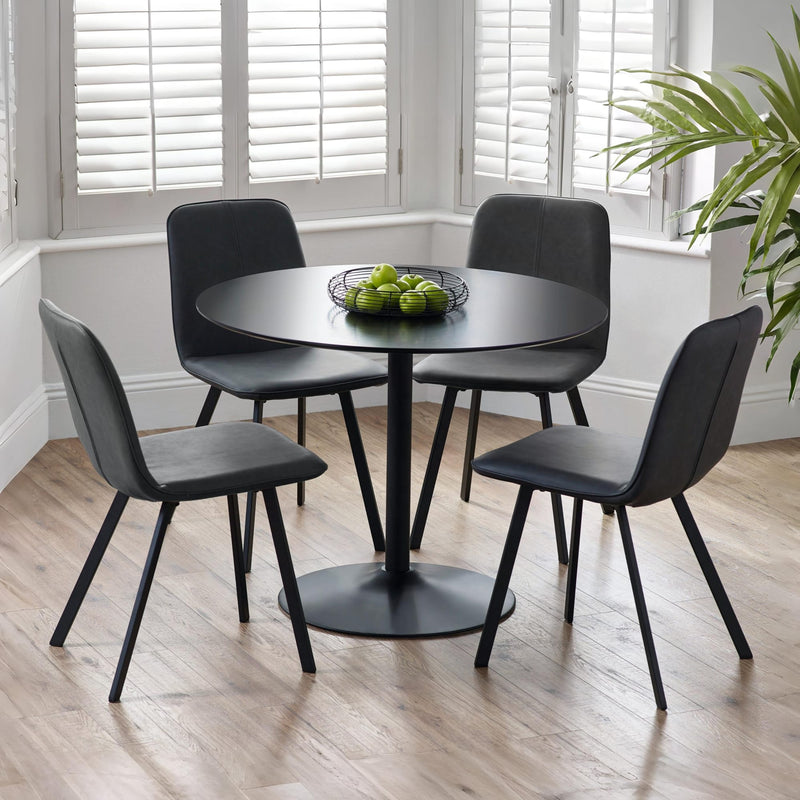 Black round dining table with four matching chairs in a room with large windows and a plant.