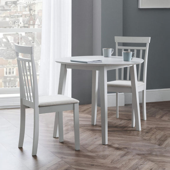 White dining table with chairs in a room with large windows and gray walls.