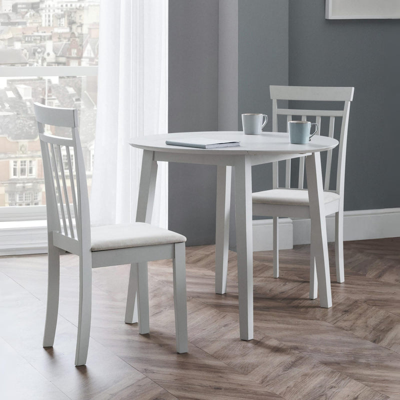 White dining table with chairs in a room with large windows and gray walls.
