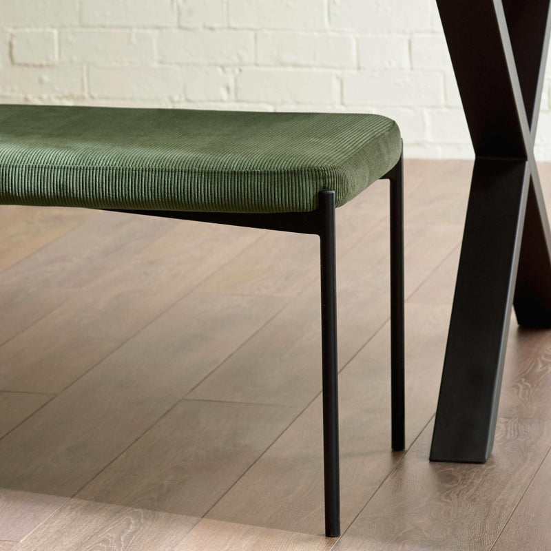 Green cushioned bench with black legs on a wooden floor.