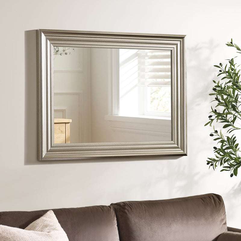 Decorative wall mirror with a silver frame on a white wall above a sofa.