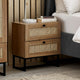 Wooden nightstand with wicker drawers next to a bed in a bedroom setting.