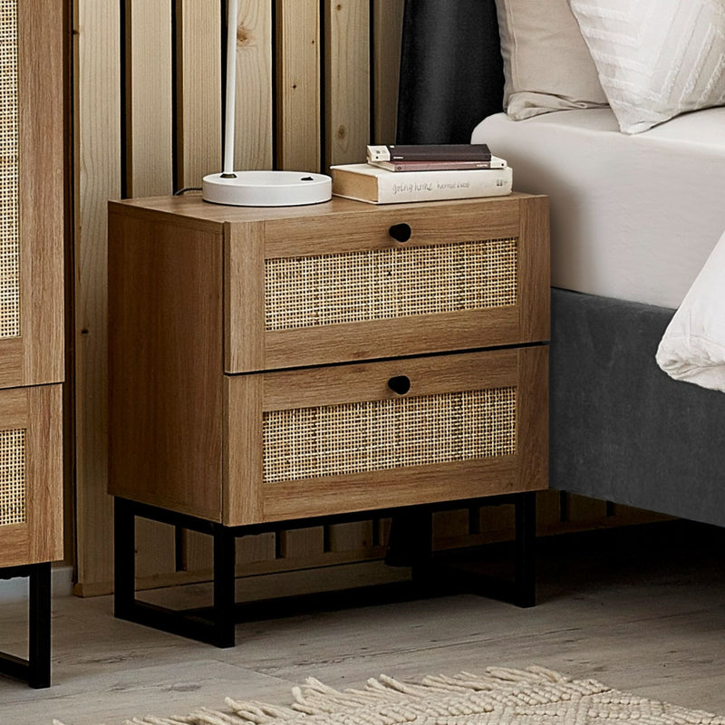 Wooden nightstand with wicker drawers next to a bed in a bedroom setting.