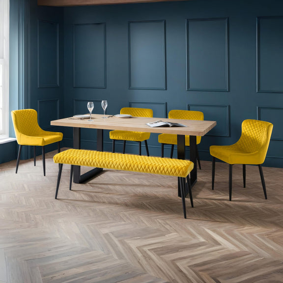 Modern dining area with yellow chairs and bench against a blue paneled wall.