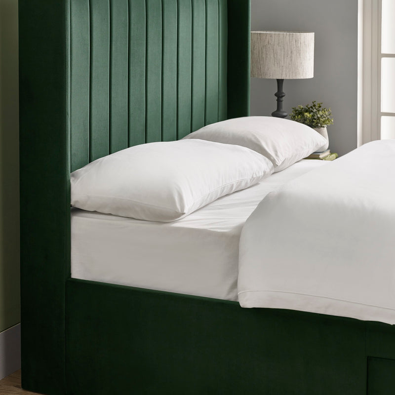 Bed with white bedding and pillows against a dark green headboard.
