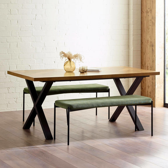 Wooden dining table with green benches against a white brick wall.