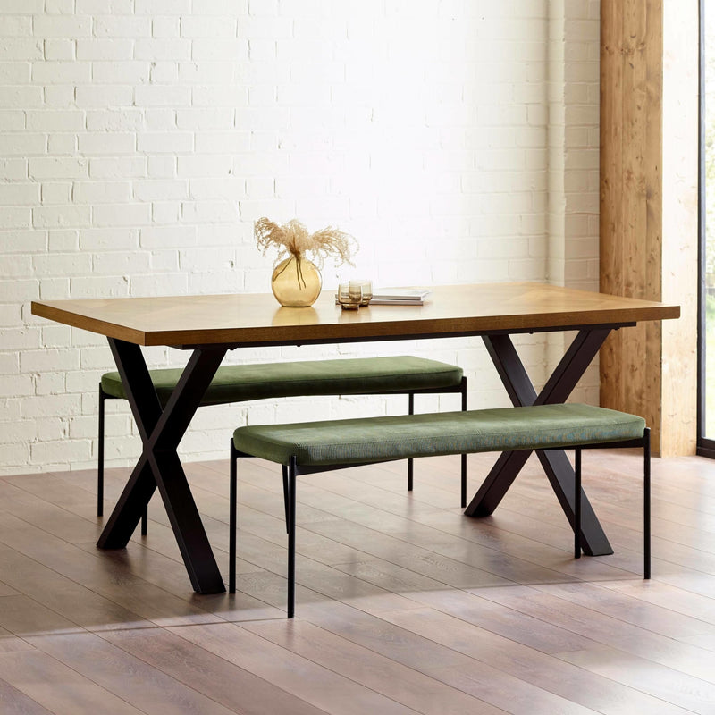 Wooden dining table with green benches against a white brick wall.
