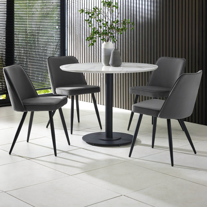 Round white table with four gray chairs in a modern indoor setting.
