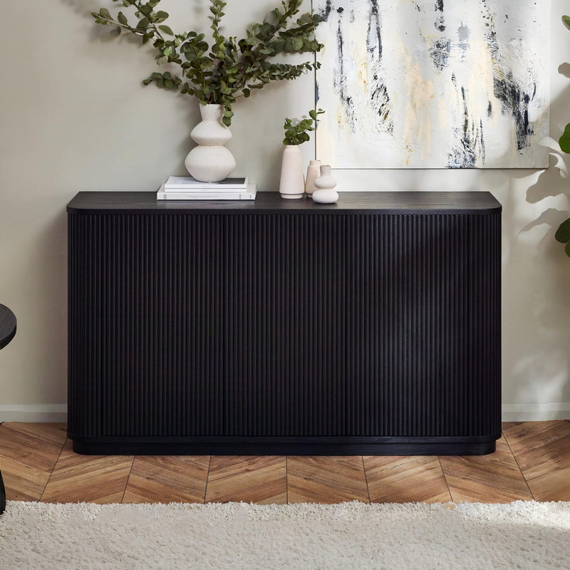 Black sideboard with decorative items in a room with a painting and plants.
