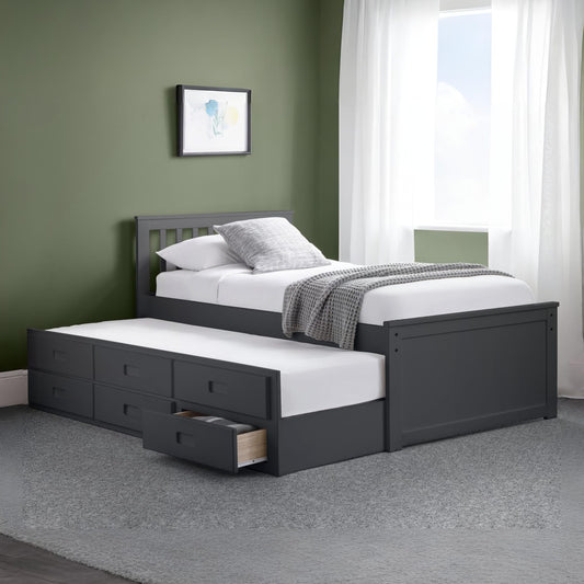 Gray bed with white bedding and pull-out drawer in a room with green walls and a window.