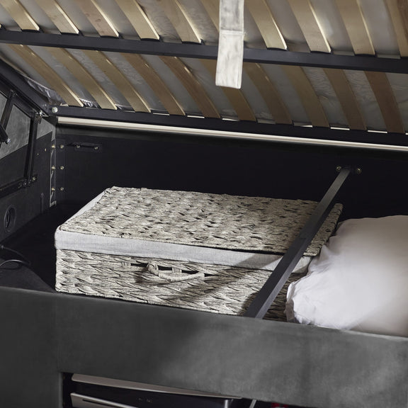 Bed with wooden box and white pillow inside a vehicle with open roof