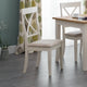 Dining room with white chairs and a wooden table against a gray wall with leaf-patterned curtains.