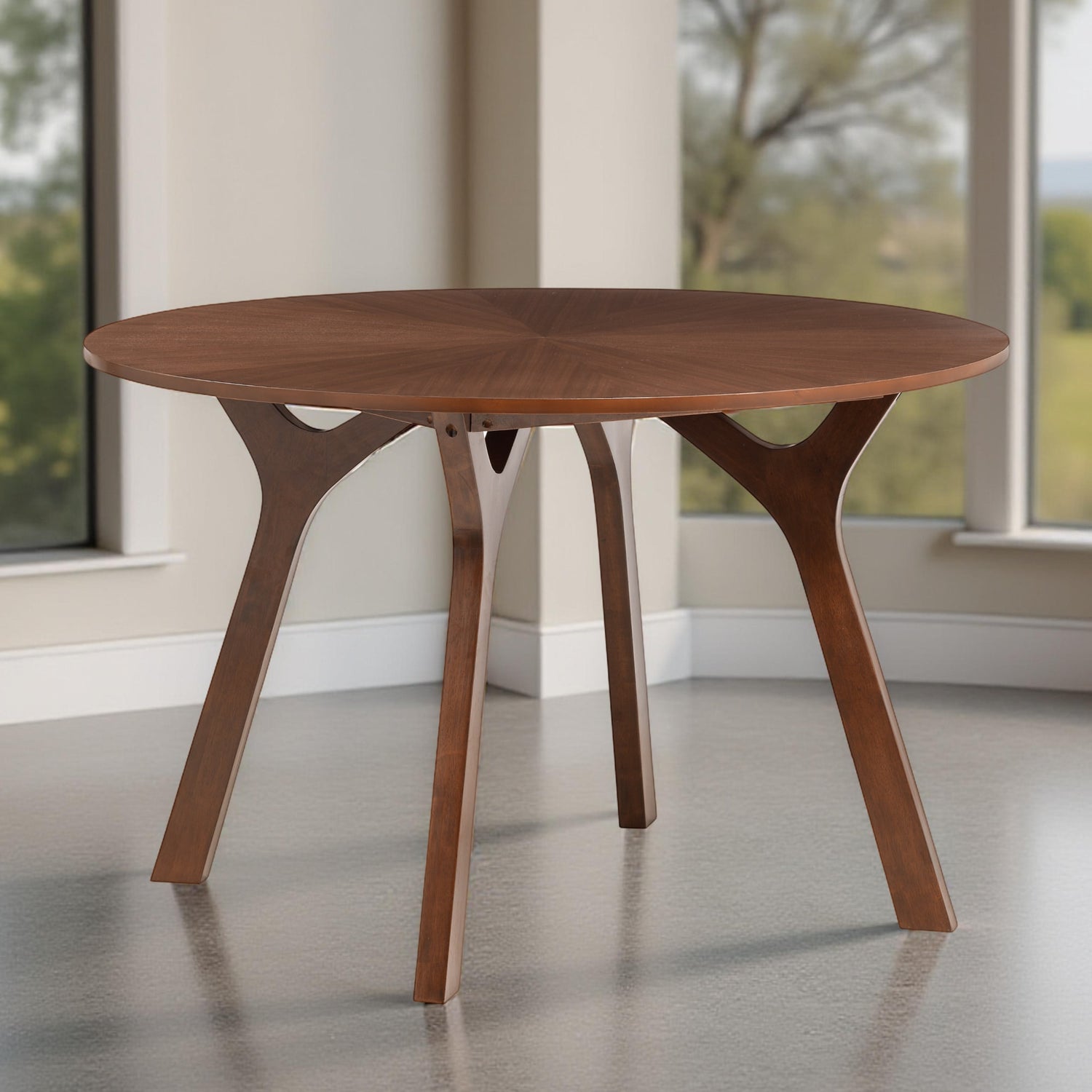 Wooden round table with unique legs in a room with large windows.