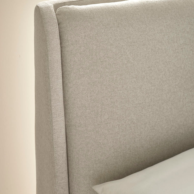 Close-up of a beige upholstered headboard with a pillow on a neutral background