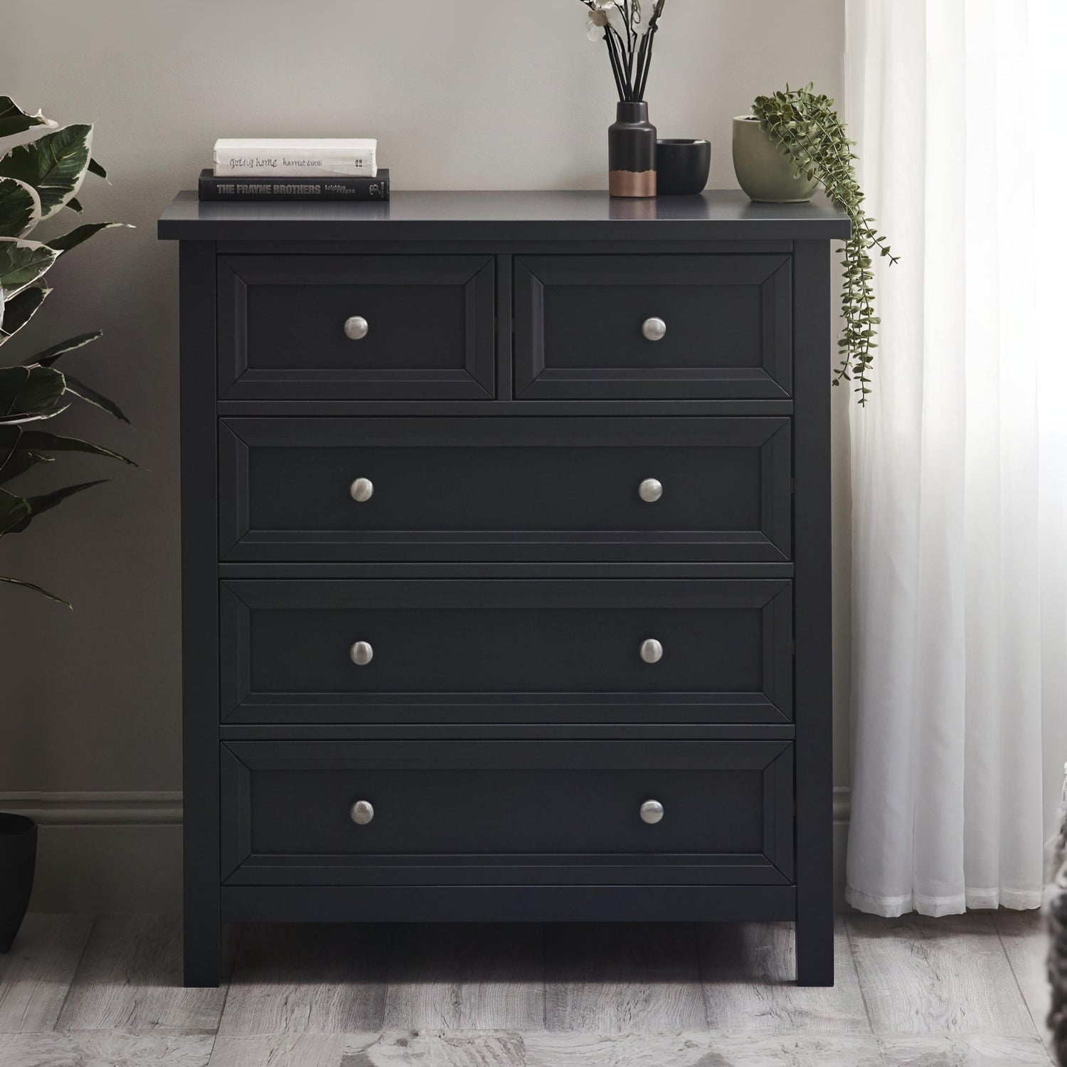 Black dresser with silver knobs in a room setting with plants and decor.