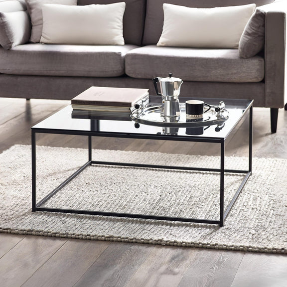 Modern living room with a glass coffee table, books, and a teapot.